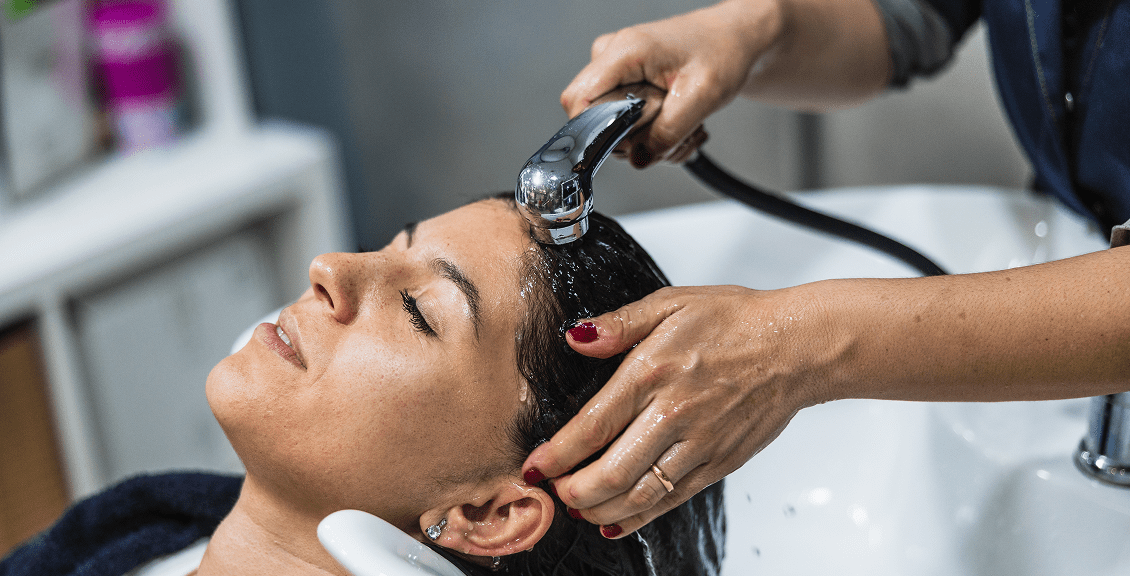 Hairdresser washing client's hair at sink